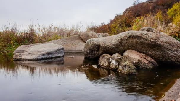 Herfstbomen en grote stenen rotsblokken. Een waterval in de herfst kreek met gevallen bladeren. Er stroomt water rond de stenen in de rivier. Aktovsky Canyon, Oekraïne. — Stockvideo