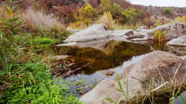 Herfstbomen en grote stenen rotsblokken. Een waterval in de herfst kreek met gevallen bladeren. Er stroomt water rond de stenen in de rivier. Aktovsky Canyon, Oekraïne. — Stockvideo