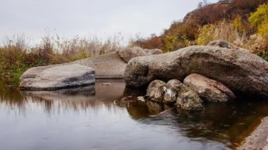 Etrafta sonbahar ağaçları ve büyük taş kayalar var. Sonbahar deresinde dökülen yapraklarla dolu bir şelale. Nehirdeki taşların etrafında su akıyor. Aktovsky Kanyonu, Ukrayna.