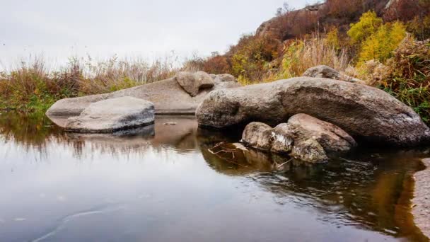 Árboles otoñales y grandes rocas de piedra alrededor. Una cascada de agua en otoño arroyo con hojas caídas. El agua fluye alrededor de las piedras del río. Aktovsky Canyon, Ucrania. — Vídeos de Stock