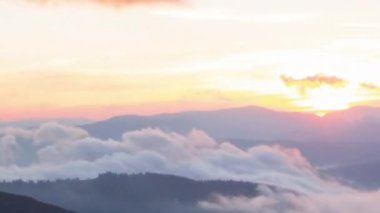 Dağlarda romantik renkli gündoğumu. Güneş doğar, mavi ve turuncu bulutlar gökyüzünde akar. Muhteşem muhteşem bir manzara. Yavaş çekim süresi 4K görüntüsü.
