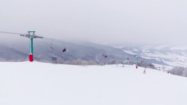 Sífelvonók a háttérben hófödte hegyek és egy hegyi gleccser. Üres egyszemélyes székek fel-le mozognak a felvonón. Síelők, snowboardosok és turisták jöttek a hétvégére a turizmusért — Stock videók