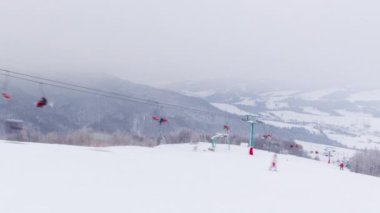 Kar kaplı dağların arka planında kayak kaldırımları ve bir dağ buzulu. Sandalyeler asansörde bir aşağı bir yukarı hareket ediyor. Hafta sonu turizm için kayakçılar, snowboardcular ve turistler geldi.