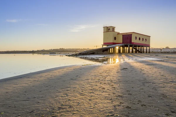 Pôr-do-sol e edifício histórico de guarda-vidas em primeiro plano, na vila piscatória de Fuseta, parque de conservação da Ria Formosa, Algarve . — Fotografia de Stock