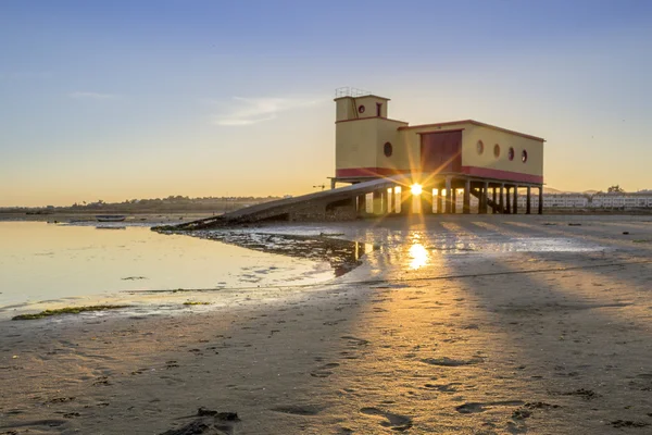 Solnedgång och historiska liv-guard byggnad i förgrunden, på Fuseta fiskeby, Ria Formosa bevarande park, Algarve. — Stockfoto