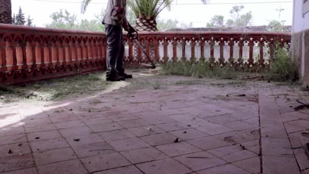 Weed string trimmer gardener, cleaning old patio in building recovery. — Stock Video