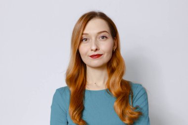 Beyaz arka planda mavi elbiseli güzel kızıl saçlı bir kadının yakın plan portresi.