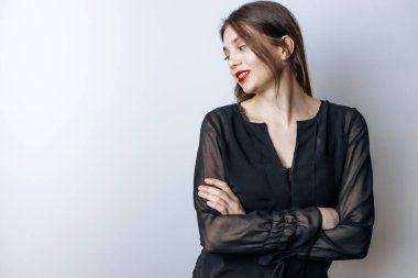 Kırmızı dudaklı ve siyah bluzlu bir kız ellerini arka planda çapraz yapıp sola bakıyor. Boşluğu kopyala
