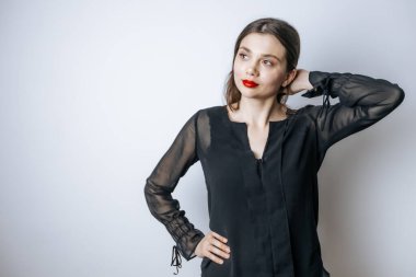 Kırmızı dudaklı esmer bir kadın açık gri arka planda kafasına dokunur.