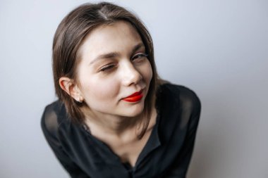 Kırmızı dudaklı güzel bir kız göz kırpıyor. Açık arkaplanda büyük bir portre