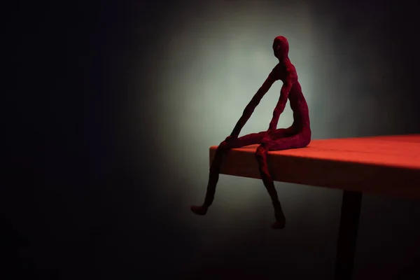 Dramatik bir adam uçurumda oturur. Siyah arkaplan ve kırmızı ışık