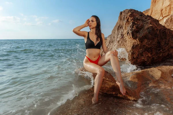 穿着红色泳衣的性感女孩正坐在海滩上 — 图库照片