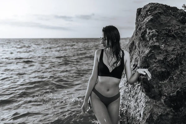 日落时一个女孩在石头边的海景上的黑白画像 — 图库照片