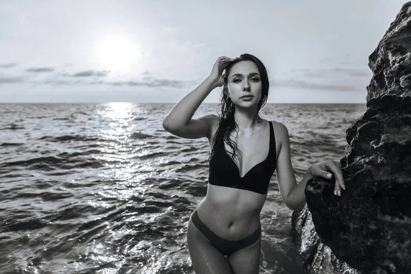 日落时一个女孩在石头边的海景上的黑白画像 — 图库照片