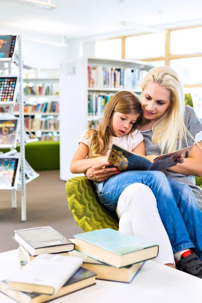 Mãe com a menina ler livro juntos na biblioteca — Fotografia de Stock