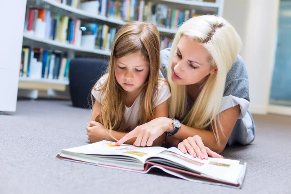 Mãe com filha ler livro juntos na biblioteca — Fotografia de Stock