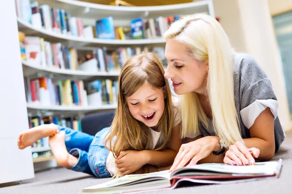 Mãe com filha ler livro juntos na biblioteca — Fotografia de Stock