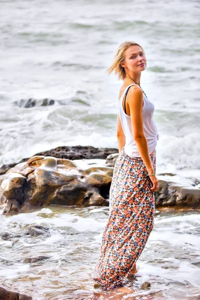 Donna bionda posa sulla riva rocciosa del mare — Foto Stock