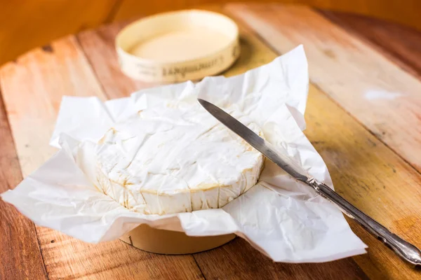 Queso Camembert envuelto en papel con cuchillo vintage en t de madera — Foto de Stock
