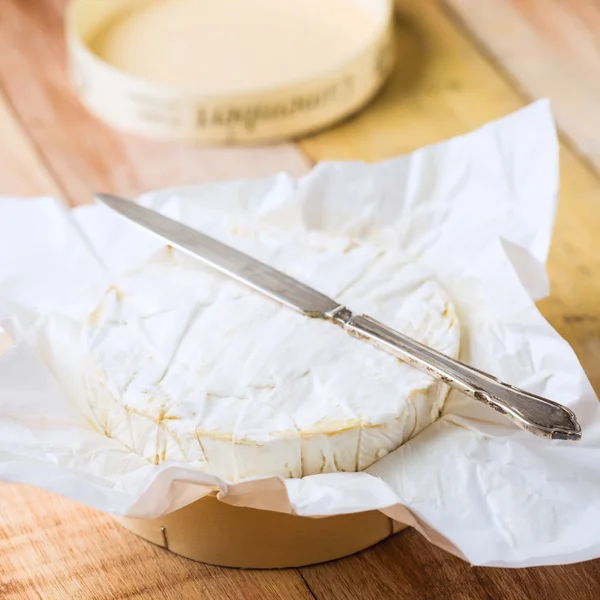 Queso Camembert envuelto en papel con cuchillo vintage en t de madera — Foto de Stock