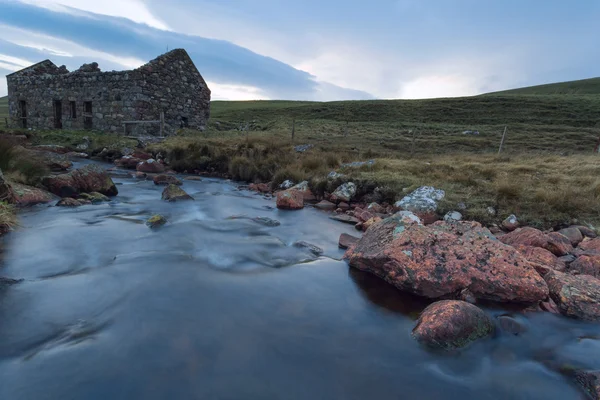 Um velho bothy arruinado em uma charneca escocesa e um riacho flui através — Fotografia de Stock