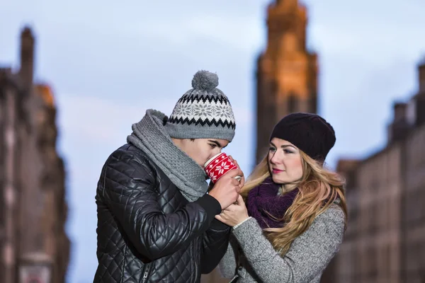 Jovem casal apaixonado abraçando e bebendo bebida quente de copo vermelho — Fotografia de Stock