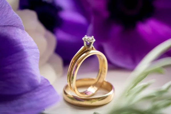 緑の白い背景に結婚指輪と紫色の花 — ストック写真