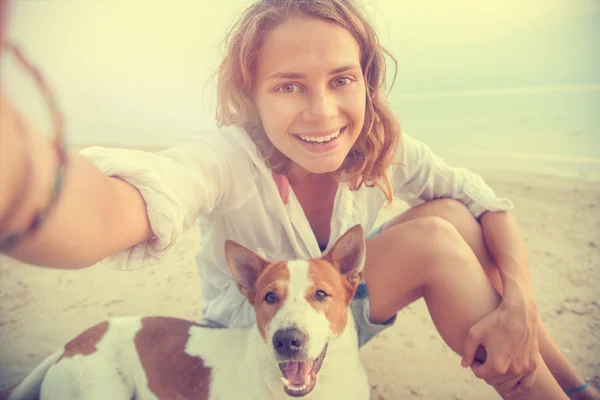 pretty young woman doing selfie with her dog on the beach at sun