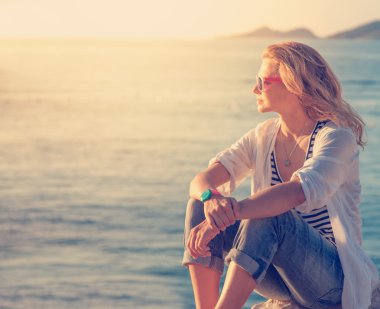 Sahilde oturan ve güneşler izlerken güzel genç kadın