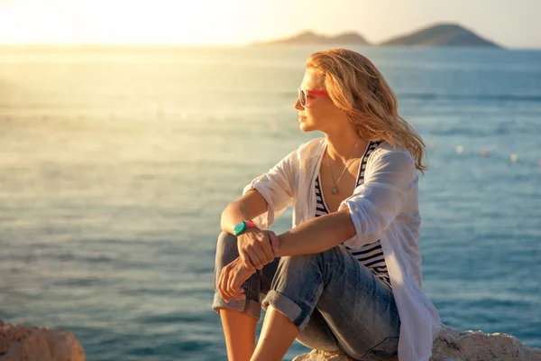 ビーチに座って太陽を見て美しいの若い女性 — ストック写真