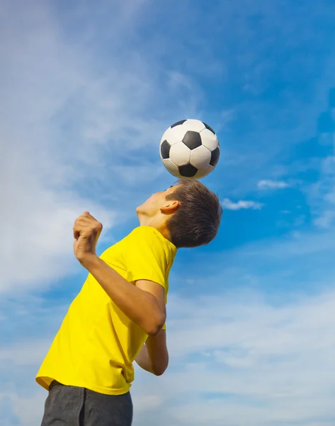 Feliz adolescente con una pelota de fútbol en la cabeza en el cielo azul bac —  Fotos de Stock