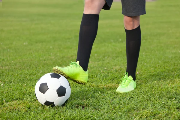 Pelota de fútbol y un jugador de fútbol piernas en un césped verde, close-u —  Fotos de Stock