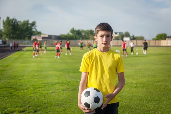Серйозний хлопчик-підліток з футбольним м'ячем в руці проти б — стокове фото