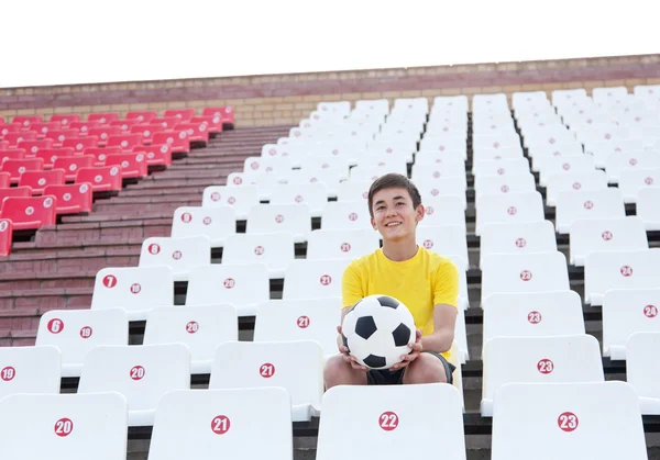 Feliz adolescente con pelota de fútbol en sus manos sentado en tribunas —  Fotos de Stock