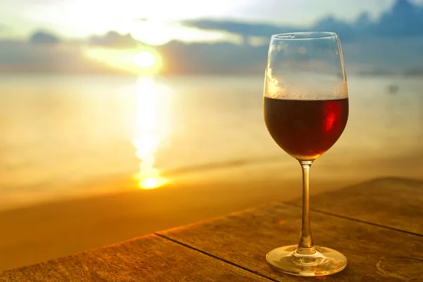 Glass of red wine  on the beach at colorful sunset — Stock Photo, Image