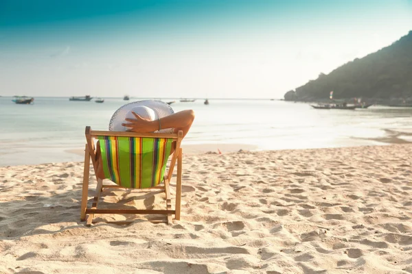 Mujer en un sombrero en una playa, sentada en una tumbona y mirando — Foto de Stock