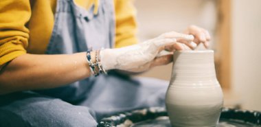 Kadın çömlekçi çarkında çömlek yapıyor, elleri kilden yakın plan.