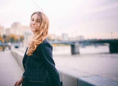 Ceketinde gür kıvırcık saçları olan güzel genç bir kadın şehrin sokaklarında neşeyle gülüyor.