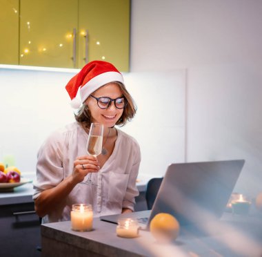 Noel Baba şapkalı güzel, genç ve mutlu bir kadın yılbaşını ve internetteki yılbaşını elinde cam şampanyayla kutluyor..