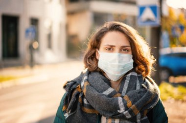 Şehir caddesinde koruyucu maske takmış güzel bir Avrupalı kadının portresi. Pandemik, sağlık ve güvenlik önlemleri yeni normal bir hayat için