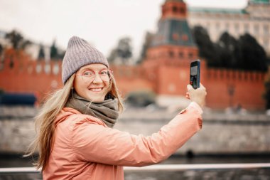Kırmızı saçlı, gözlüklü, şapkalı, ceketli, akıllı telefonlu bir kadın Moskova 'da selfie çekiyor.