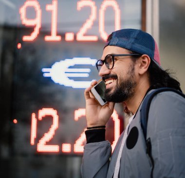 Şapkalı çekici genç esmer adam döviz bürosunun arka planında cep telefonuyla konuşuyor.