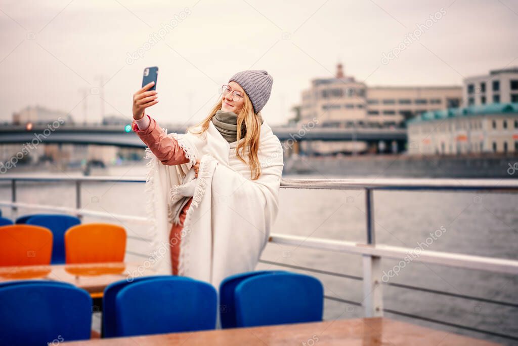 Young woman in glasses traveler in a hat and jacket making a selfie in Moscow on a pleasure boat on the river in center