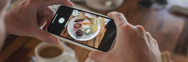 Photo of food on a smartphone in a cafe, male hands take a picture of breakfast of scrambled eggs.
