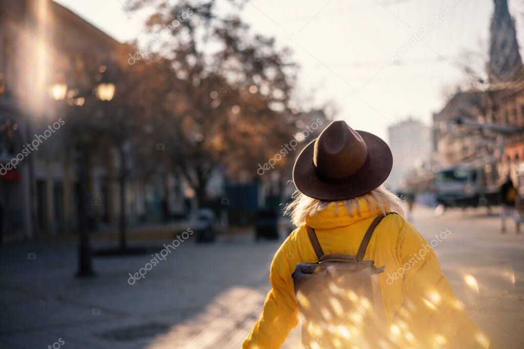 Young woman traveler in yellow jacket and hat walking in a european city on a sunny day