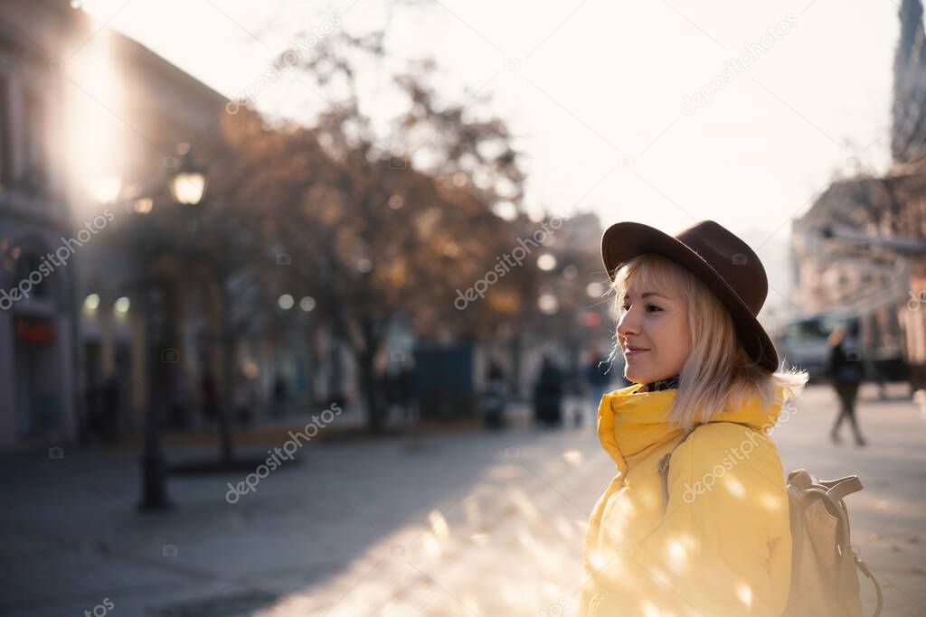 Young woman traveler in yellow jacket and hat walking in a european city on a sunny day