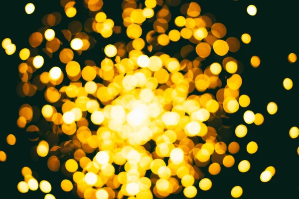 Yellow shining gold glare bokeh on dark background, festive background and texture