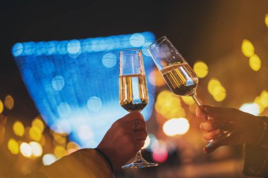 Bir Avrupa şehrinin gece sokaklarında elinde şampanya bardaklarıyla iki kadın eli, tatil kavramı.