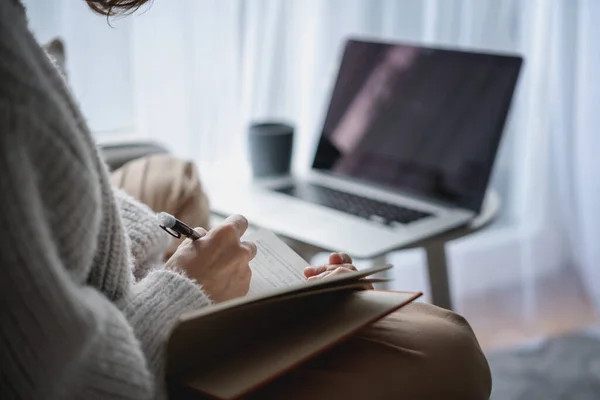 Manos femeninas haciendo notas en un cuaderno frente a la pantalla del ordenador portátil, educación en línea y concepto de trabajo — Foto de Stock