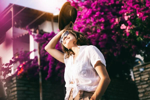 帽子とサングラスで白いシャツの美しい若いスタイリッシュな女性旅行者の女の子は夏の日に歩く — ストック写真